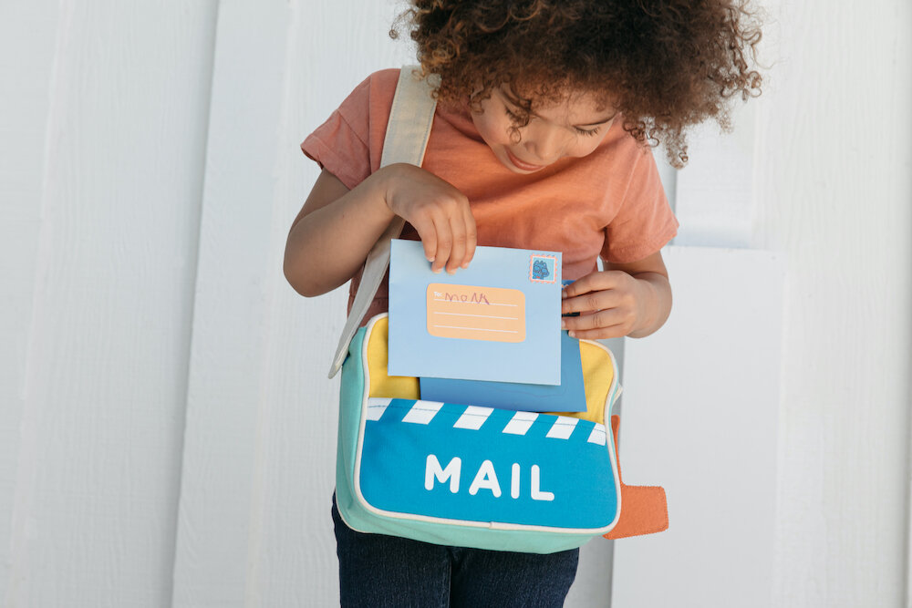 Child placing pretend mail into a bag