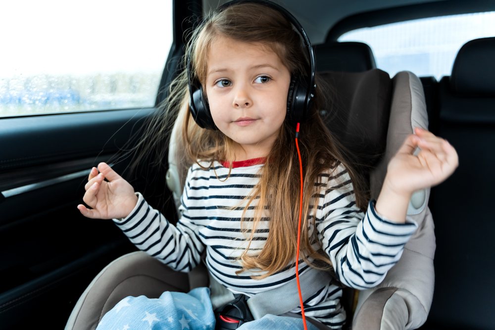 Young girl listening to music and dancing in car seat