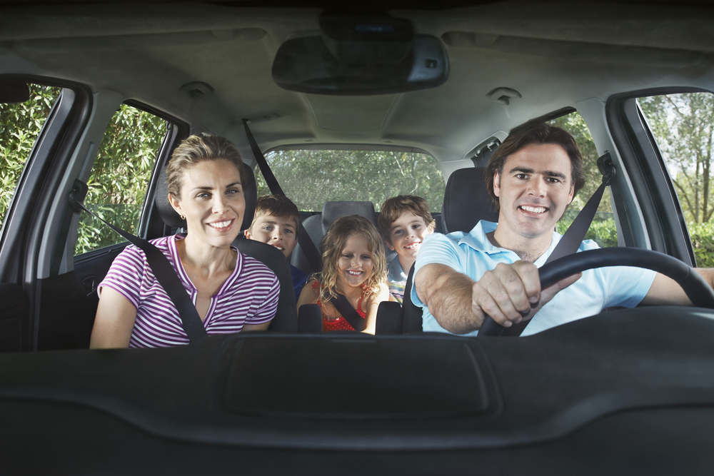 Family sitting in car wearing seatbelts, smiling at camera