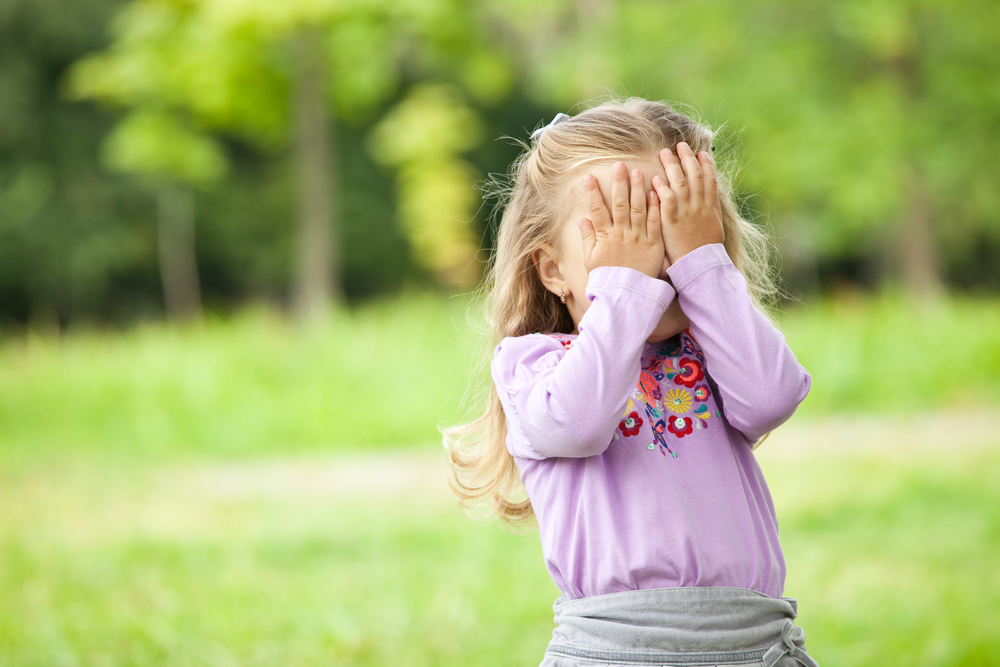 Shy kid holding hands over her eyes outside