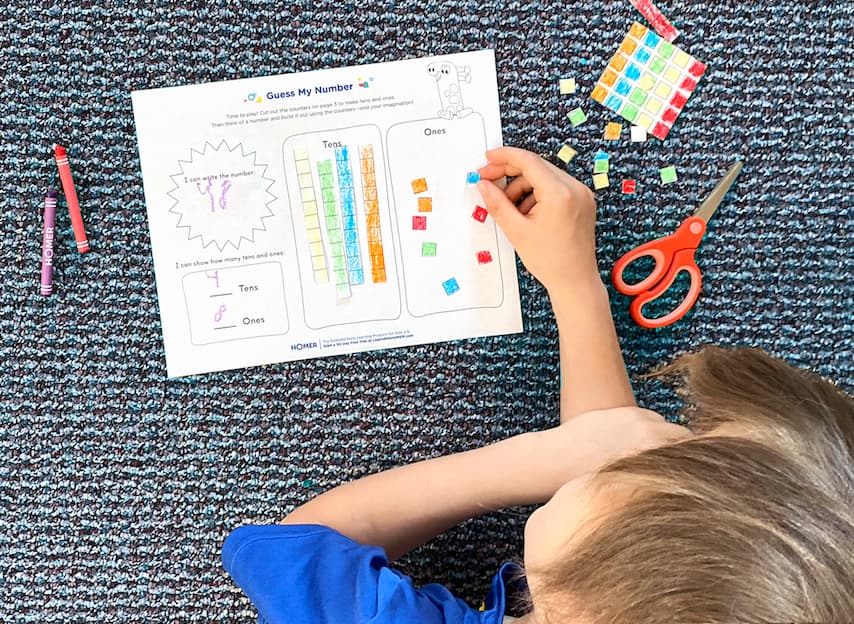 Child working on Guess My Number printable on floor, with crayons and scissors
