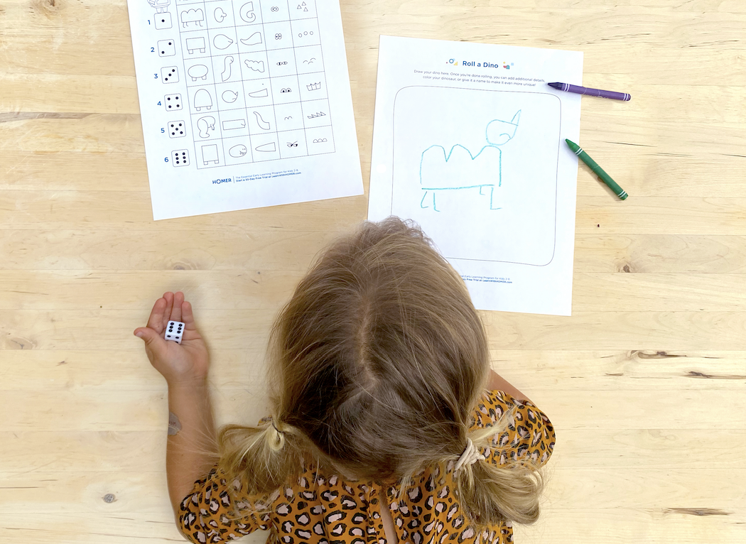 Child on floor rolling die with two printed out roll-a-dino sheets and crayons