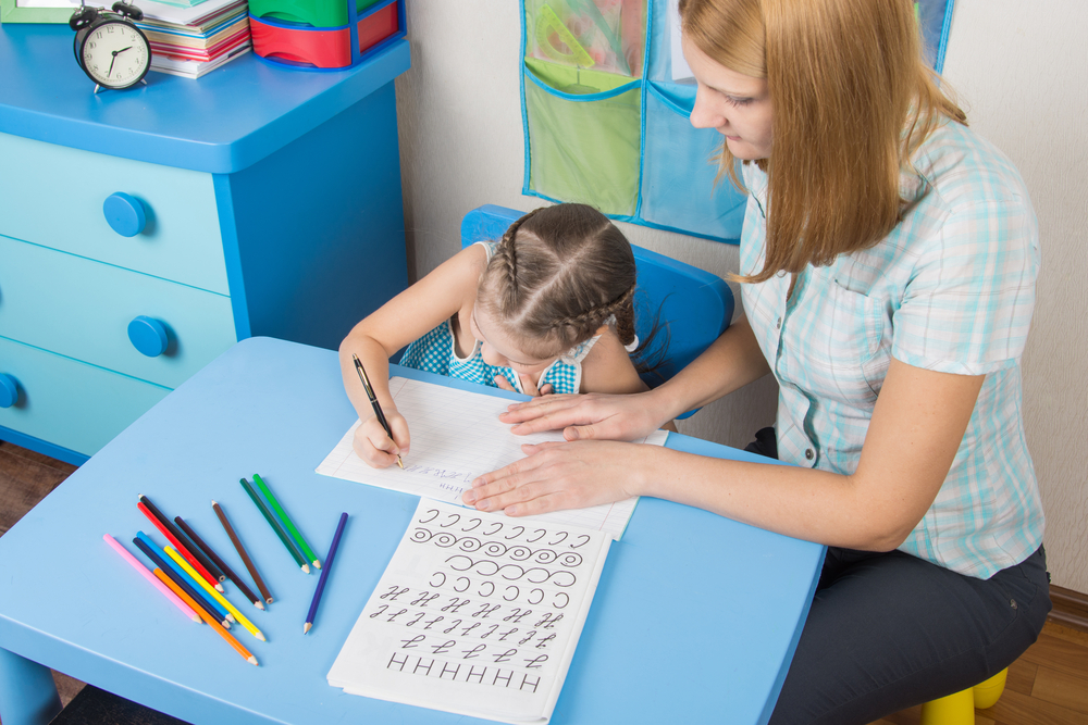 Child practicing letters with help from mentor