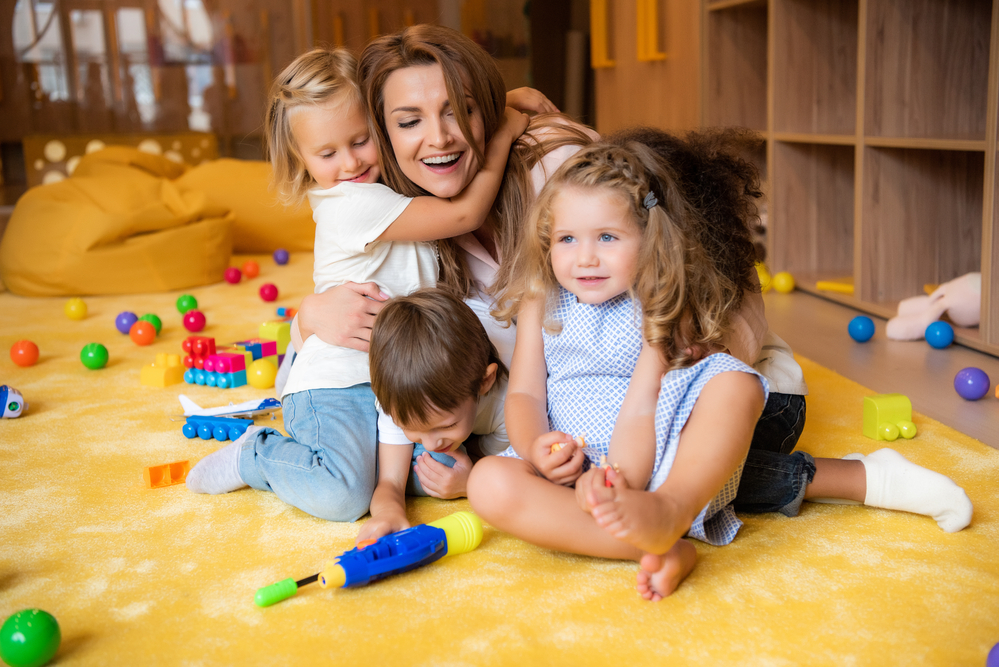 Mom with 3 kids playing on floor with lots of toys