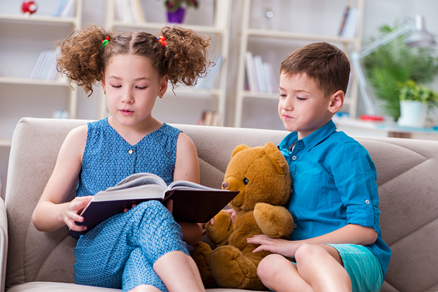 Two kids on coach doing Kindergarten teacher helping student with Brother and sister doing kindergarten reading