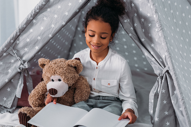 Young girl in tent holding teddy bear and working on her kindergarten reading skills