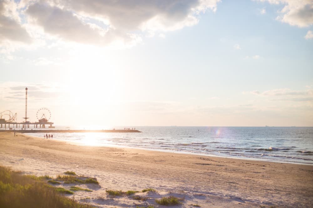 Sunrise over the beach in Galveston, Texas, with a pier filled with carnival rides in the background