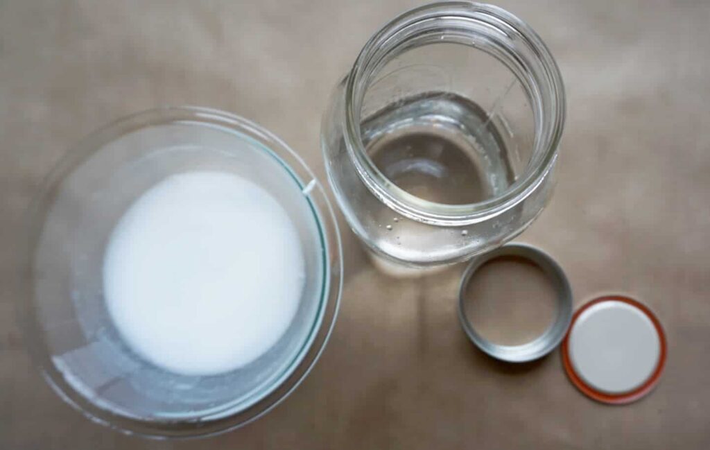Mason jar filled with baby oil and cup filled with mixture of white paint and water