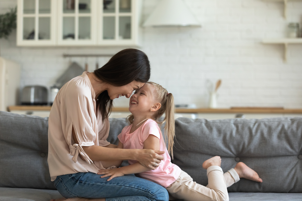Happy young woman playing with laughing little daughter on sofa